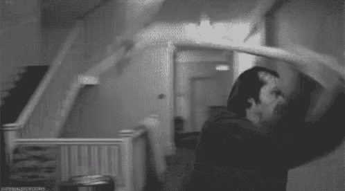 a black and white photo of a man and woman kissing in a room with stairs .