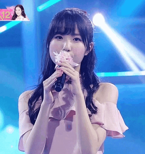 a girl in a pink dress singing into a microphone with the number 12 in the background
