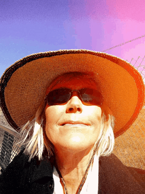 a woman wearing a straw hat and sunglasses smiles for the camera