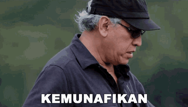 a man wearing a black hat and sunglasses has the word kemunafikan written below him