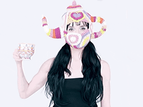 a woman wearing a colorful knitted hat holds a cup