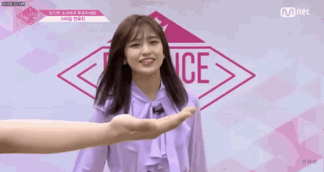 a woman in a purple shirt is being held by someone 's hand in front of a mnet logo .