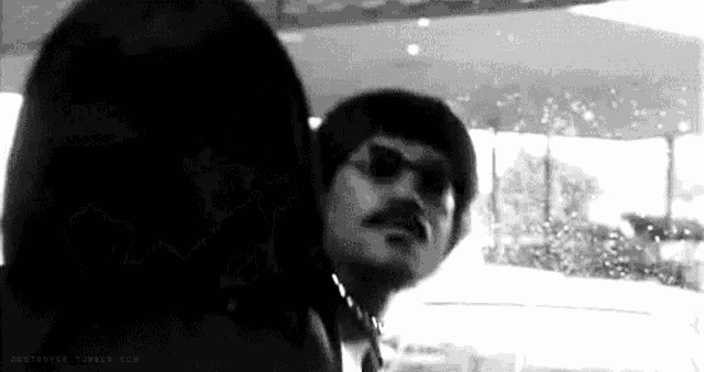 a black and white photo of a man with a mustache and sunglasses looking at another man .