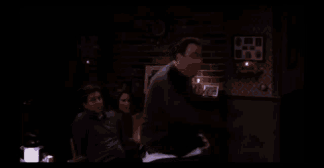 a man is dancing in a dark room with a brick wall behind him
