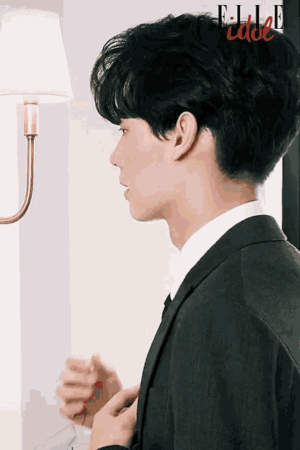 a man in a suit is standing in front of a lamp with elle idol written on the bottom right