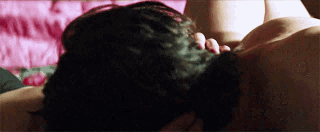 a man and a woman are kissing on a bed with a pink blanket