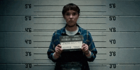 a man in a blue plaid shirt is holding up a mugshot