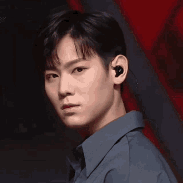 a young man wearing a blue shirt and ear buds looks at the camera .