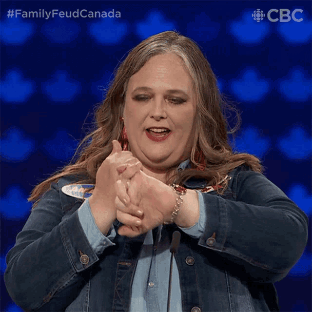 a woman wearing a denim jacket is clapping her hands in front of a blue background with the words family feud canada on it
