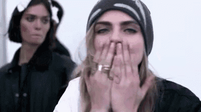a woman in a hat is covering her mouth with her hands .