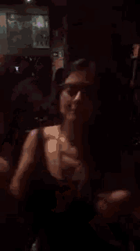 a woman wearing glasses is dancing in a dark room with other people .