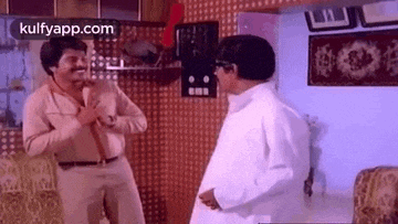two men are standing next to each other in a living room and talking .