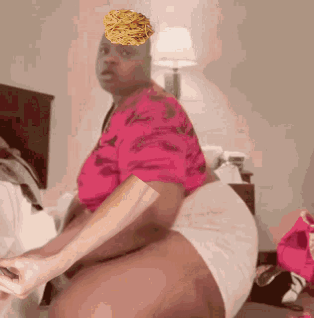 a woman in a pink shirt is sitting on a bed with french fries on her head