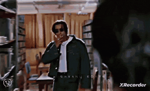 a man is smoking a cigarette in a room while wearing sunglasses and a jacket .