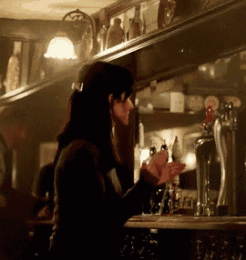 a woman is standing behind a bar holding a glass