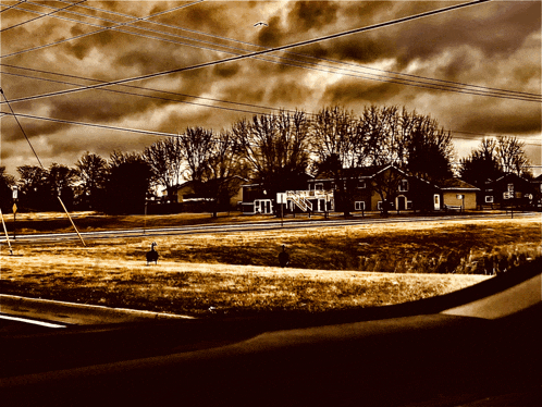 a dark cloudy sky over a residential area with a few houses and trees