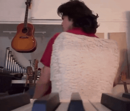 a man playing a piano with a guitar hanging from the ceiling behind him