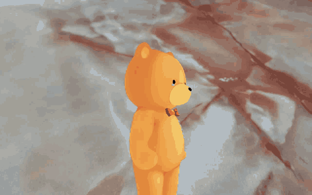 an orange teddy bear with a red bow tie stands on a marble surface