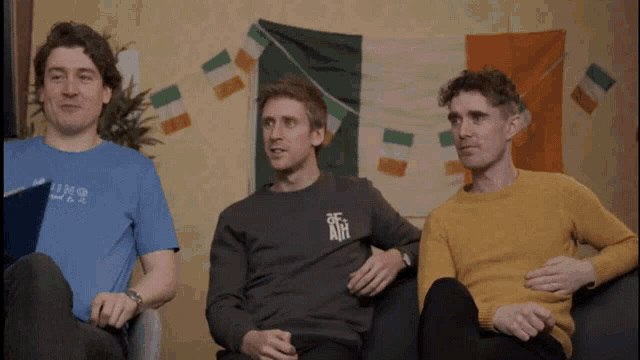 three men are sitting on a couch with one wearing a sweater that says of air