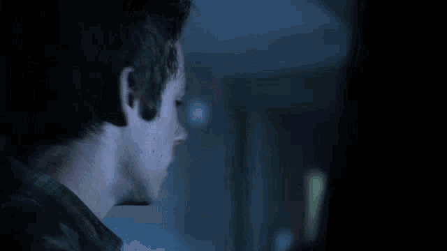 a close up of a man 's face in a dark room looking at something .