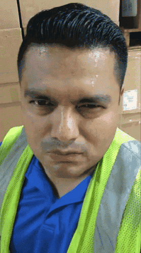 a man wearing a yellow vest and a blue shirt is making a funny face