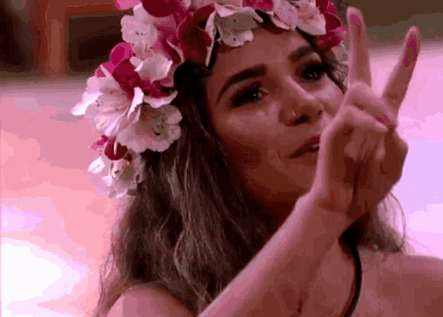 a woman with a flower crown on her head giving the peace sign