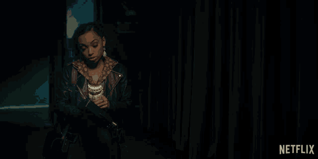 a woman in a leather jacket is standing in front of a green curtain with the words what on it