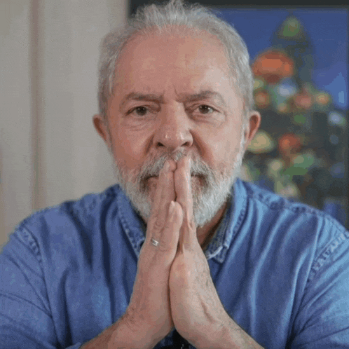 a man with a beard and a blue shirt has his hands folded in front of his face