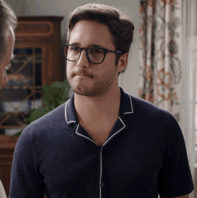 a man wearing glasses and a blue shirt looks to the side