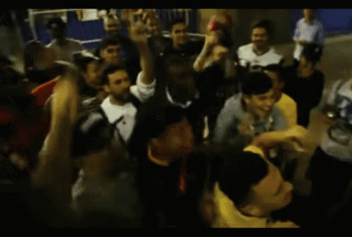 a crowd of people are dancing in a room with a blue wall behind them