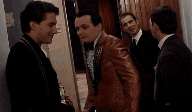 three men in suits and ties are standing in a hallway with a sign on the wall that says no smoking