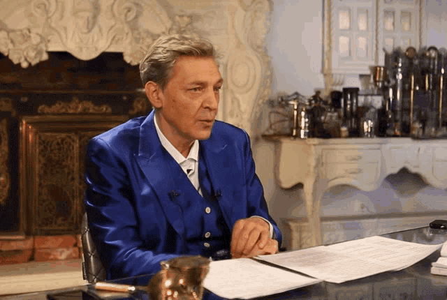 a man in a blue suit sits at a desk with papers in front of him
