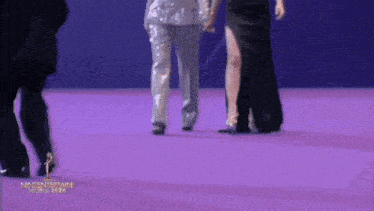 a group of people are walking on a purple carpet with a trophy in the background .