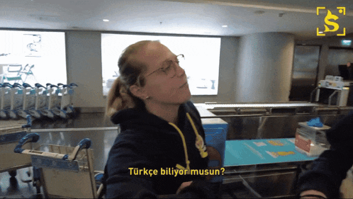 a woman wearing glasses and a black hoodie is talking to someone in a foreign language