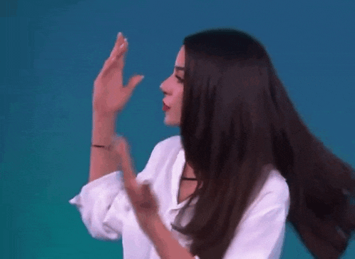 a woman with long dark hair is wearing a white shirt and making a funny face .