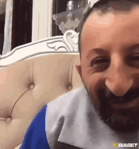 a man with a beard is sitting on a couch smiling