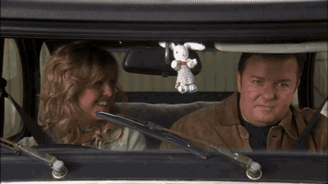 a man and a woman in a car with a stuffed bunny on the rear view mirror