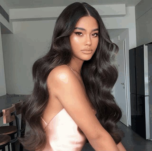 a woman with long dark hair is wearing a pink top