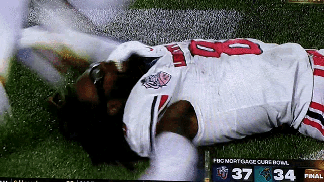 a football player is laying on the field during the mortgage cure bowl game