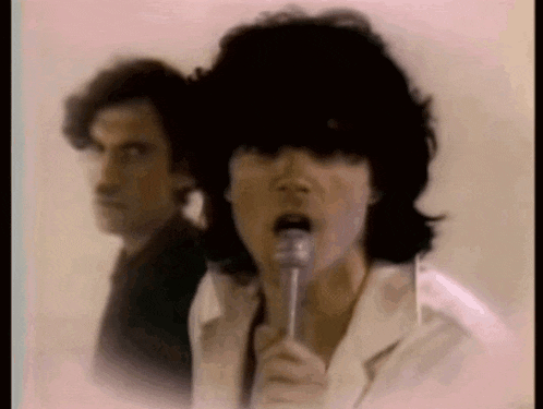 a man is singing into a microphone while another man looks on