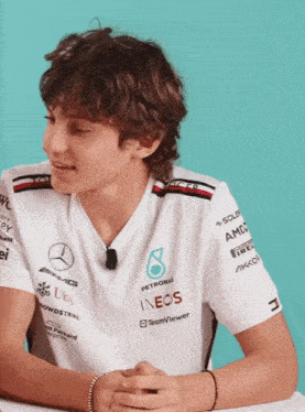 a young man wearing a petronas shirt sits at a desk