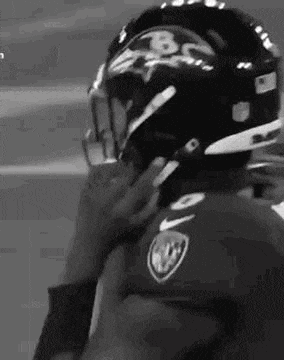 a black and white photo of a football player putting on his helmet .