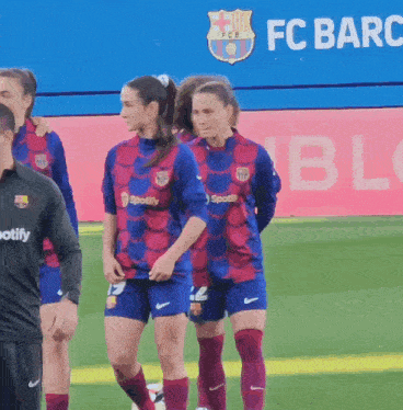 a group of female soccer players are walking on a field in front of a fc barc banner
