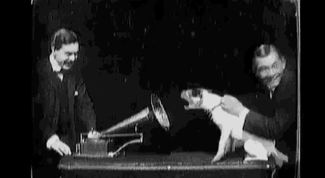 a man is playing a record on a phonograph while another man watches .