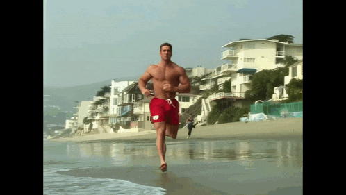a shirtless man in red swim shorts is running on the beach
