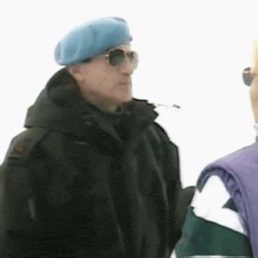 a man wearing a blue beret and sunglasses is standing in the snow