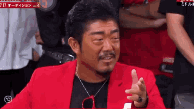 a man wearing a red jacket and glasses is talking to someone in a crowd