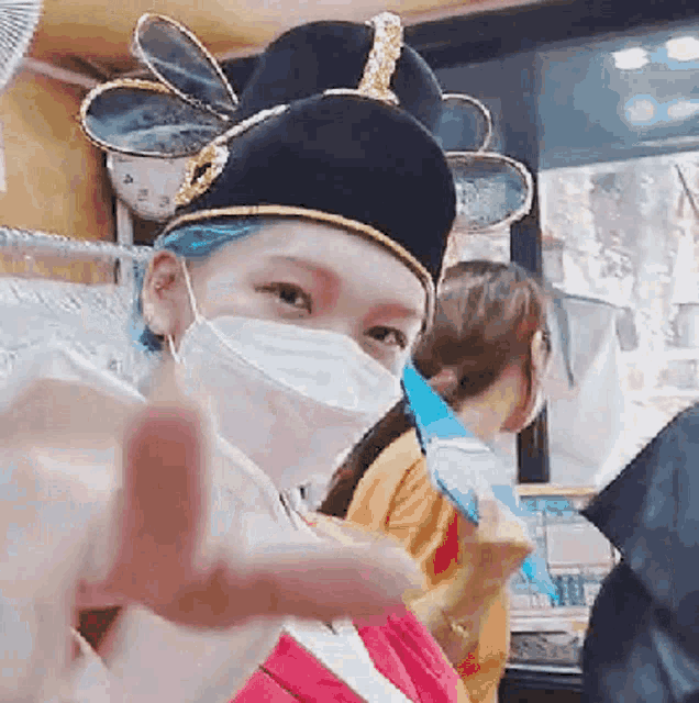 a woman wearing a mask and a hat is pointing her finger
