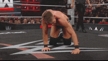a man is kneeling down in a wrestling ring with a referee in the background