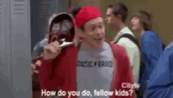 a man in a red sweater is standing in a locker room talking to a group of kids .